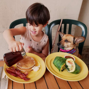 Photo of Cozmo the dog with his human cousin at Yahaira's Cafe, with a sack of pancakes and a breakfast burrito.