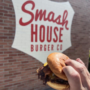 Smash burger held in hand in front of Smash House Burger Co. sign