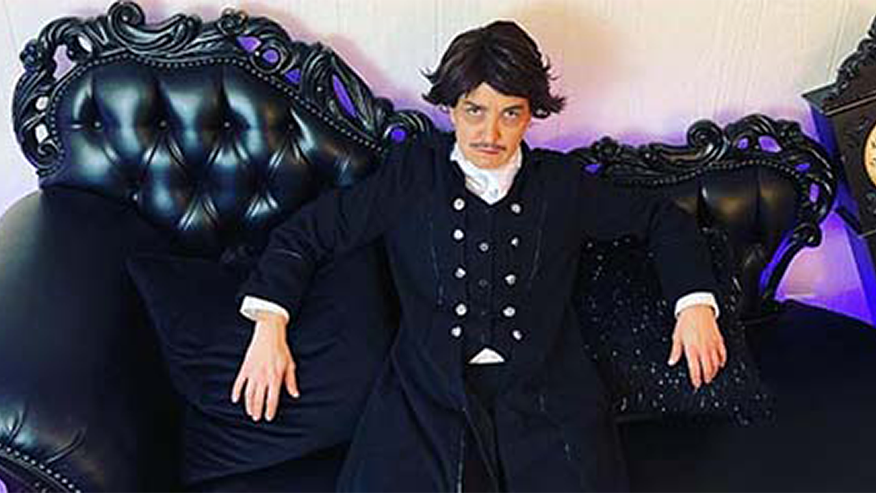 Actor portrays Edgar Allan Poe sitting on an antique black sofa