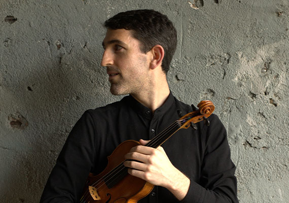 Patrick Galvin photographed holding a violin while wearing a black top.