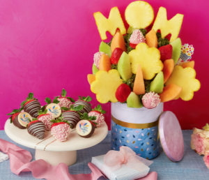 Edible arrangement made from fruits with a MOM fruit topper, next to a a platter for chocolate covered strawberries.