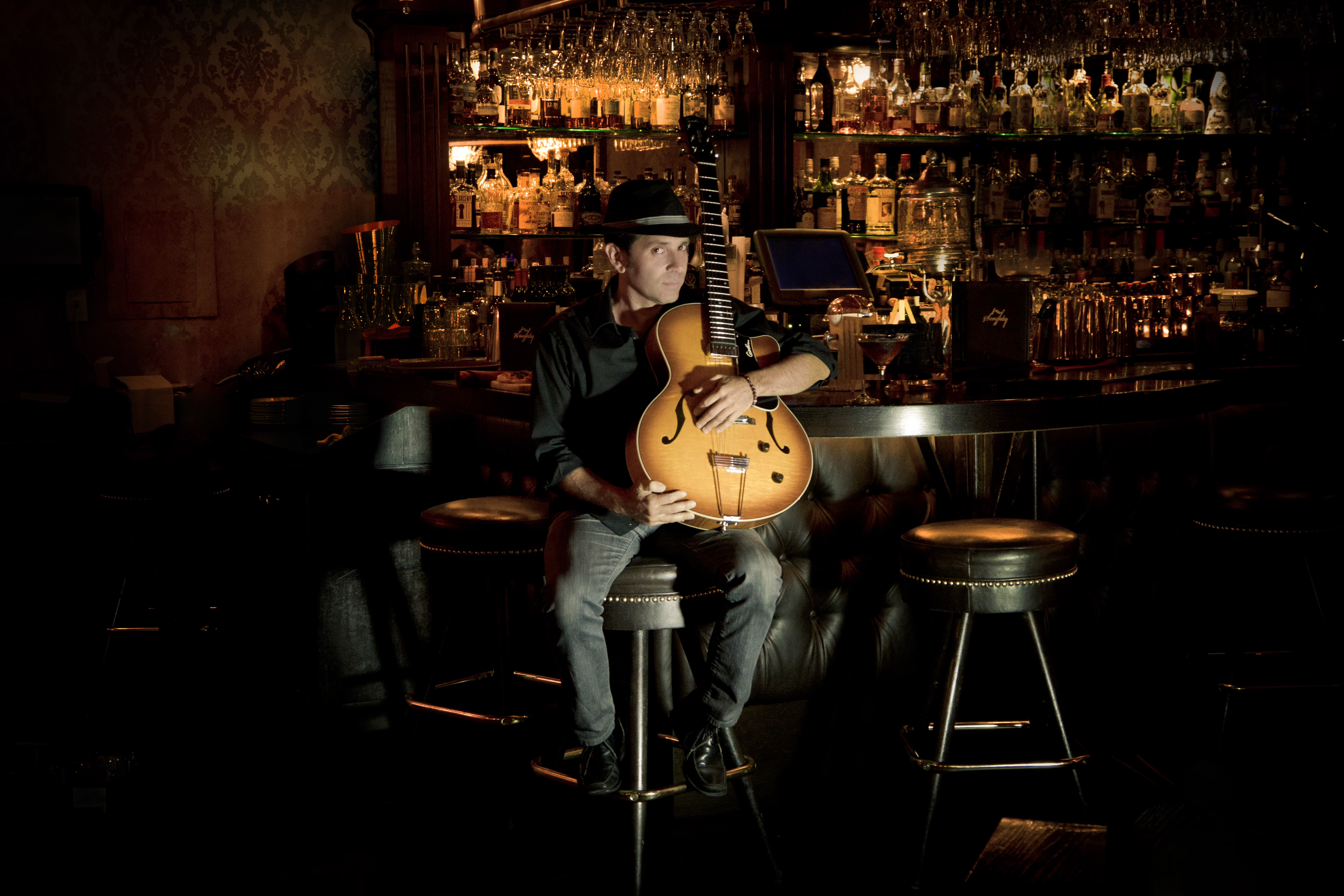 Musician Joe Lo Piccolo poses with a guitar against a dark bar background