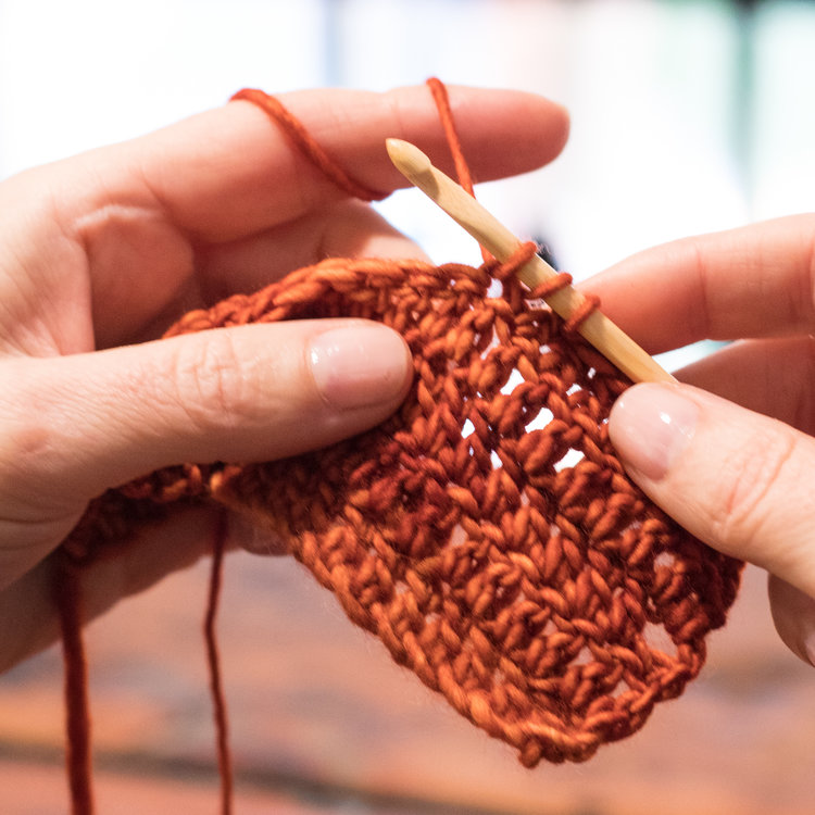 Close up of hands crocheting rows of burn orange yarn.