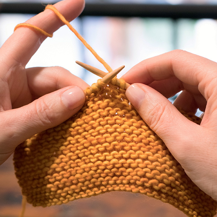 Close up of hands knitting a mustard yellow yarn.