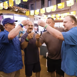 A group of four men toast with small glasses of tequila in the outdoor courtyard of El Portal restaurant.