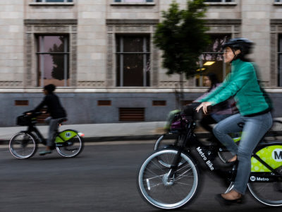 Two cyclists ride Metro Bikes down Green Street in Playhouse Village